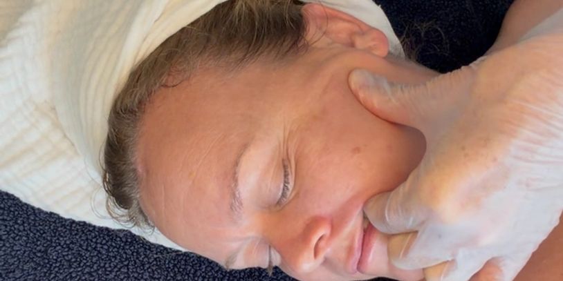 A person receiving a facial massage or therapy with gloved hands.
