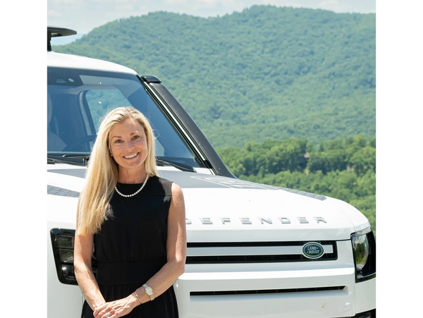 Brigid McIntyre in black dress poses confidently in front of a white Land Rover Defender in Asheville, NC where she provides luxury interior design services throughout the Asheville, NC area.