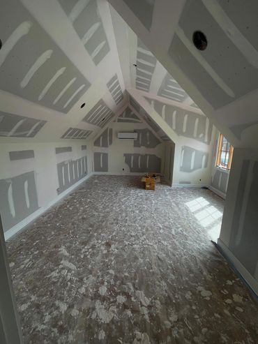 Unfinished attic room with drywall and paint splatters on floor.