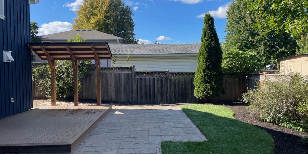 Backyard with a wooden deck, canopy, and green lawn under clear sky.