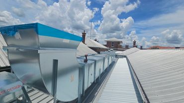 Metal air ducts installed on a rooftop under a partly cloudy sky.
