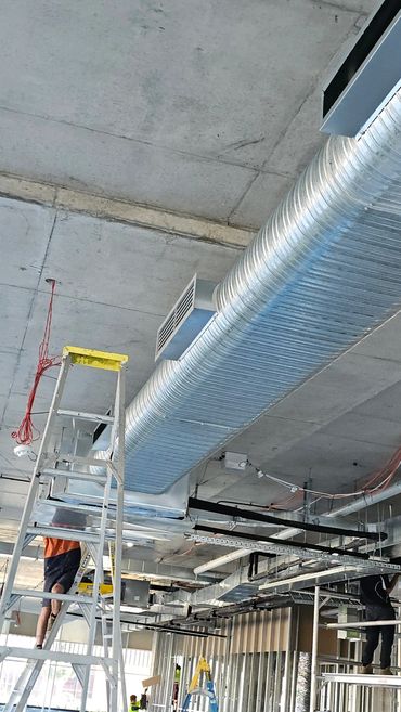 Workers install ductwork and electrical systems in a commercial building under construction.