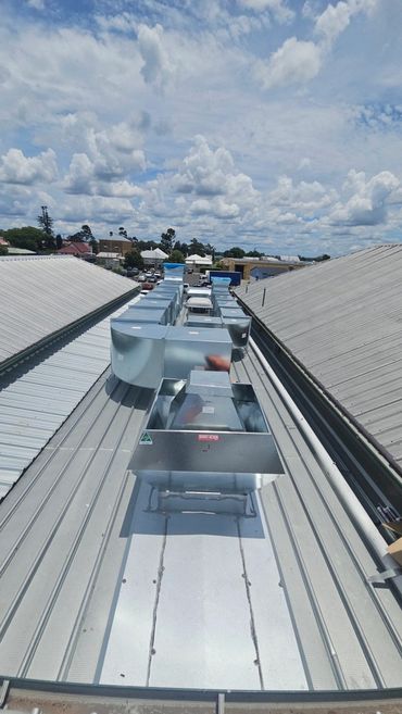 Metal ventilation ducts installed on a rooftop under a cloudy sky.