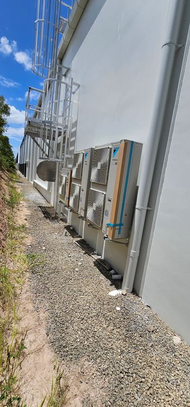 Row of air conditioning units mounted on a white building wall under a blue sky.