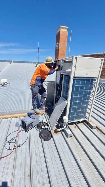 Technician repairing rooftop air conditioning unit under clear blue sky.