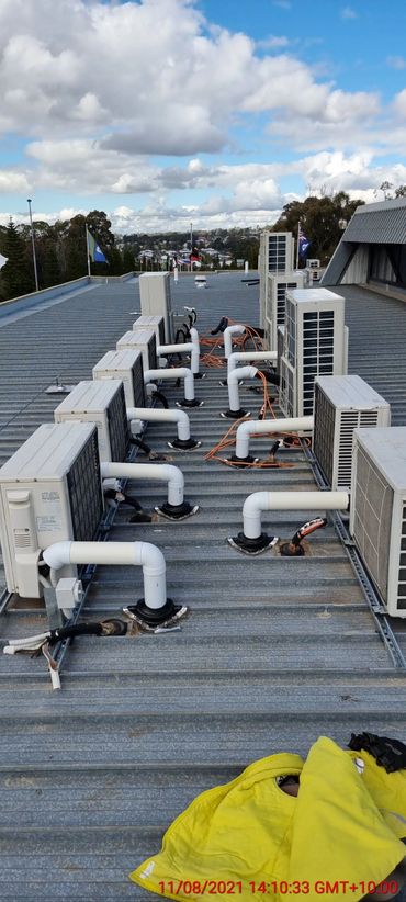 Array of air conditioning units installed on a metal rooftop under a cloudy sky.