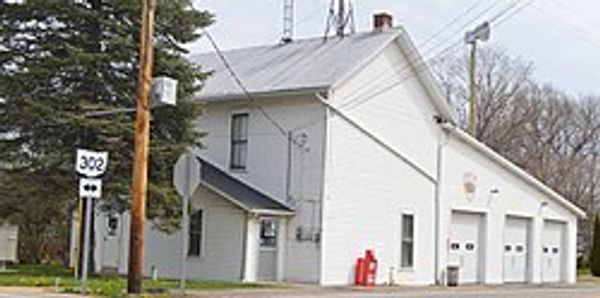White fire station building with three garage doors and a water tower in the background.