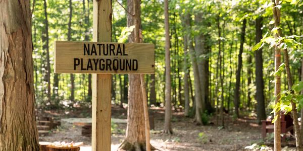A sign saying " Natural Playground" in a wooded setting for the Shelby County Parks District.