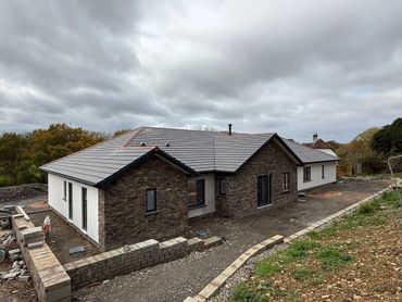 Modern house under construction with stone and white exterior walls.