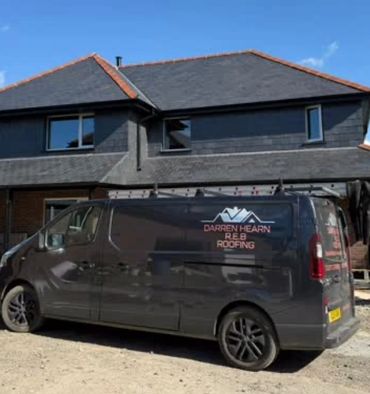 A black roofing service van parked outside a modern house with a slate roof.