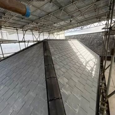 A slate roof under construction surrounded by scaffolding and protective covering.