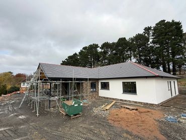 Modern house under construction with scaffolding and construction materials outside.