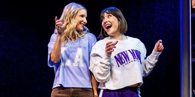 Two women smiling and dancing together on stage.