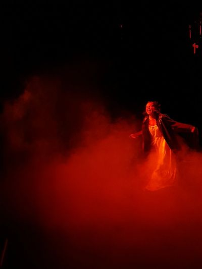 A performer in a nightgown shouting dramatically while surrounded by red smoke.