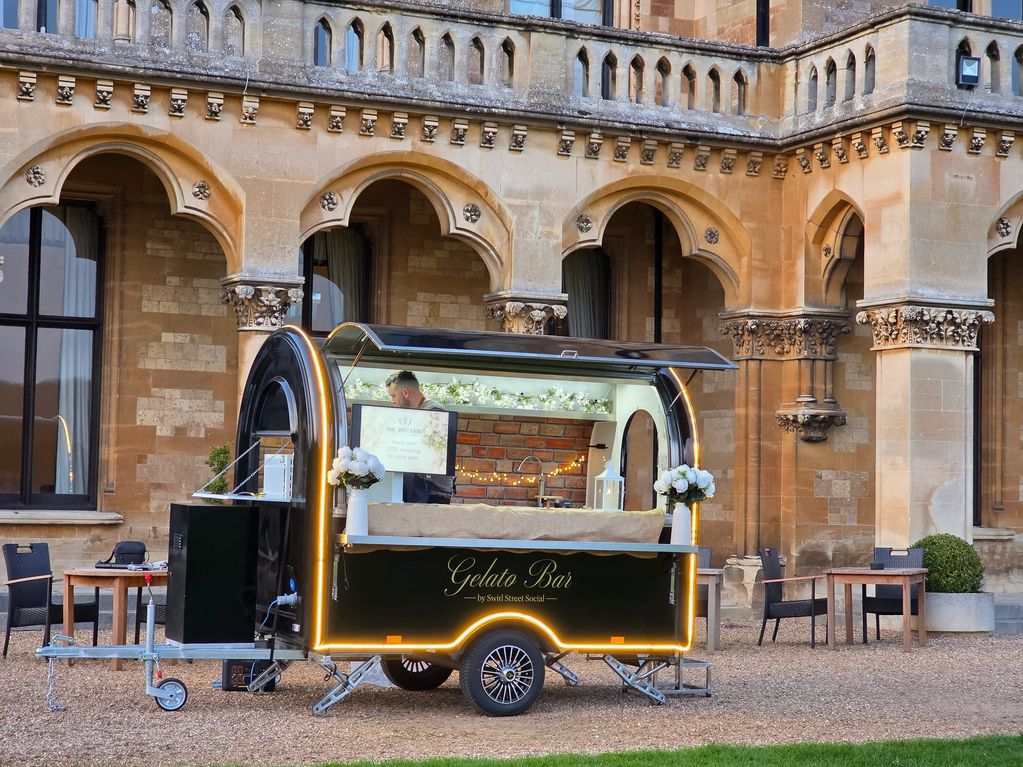 A gelato bar cart outside a historic building with arched windows.