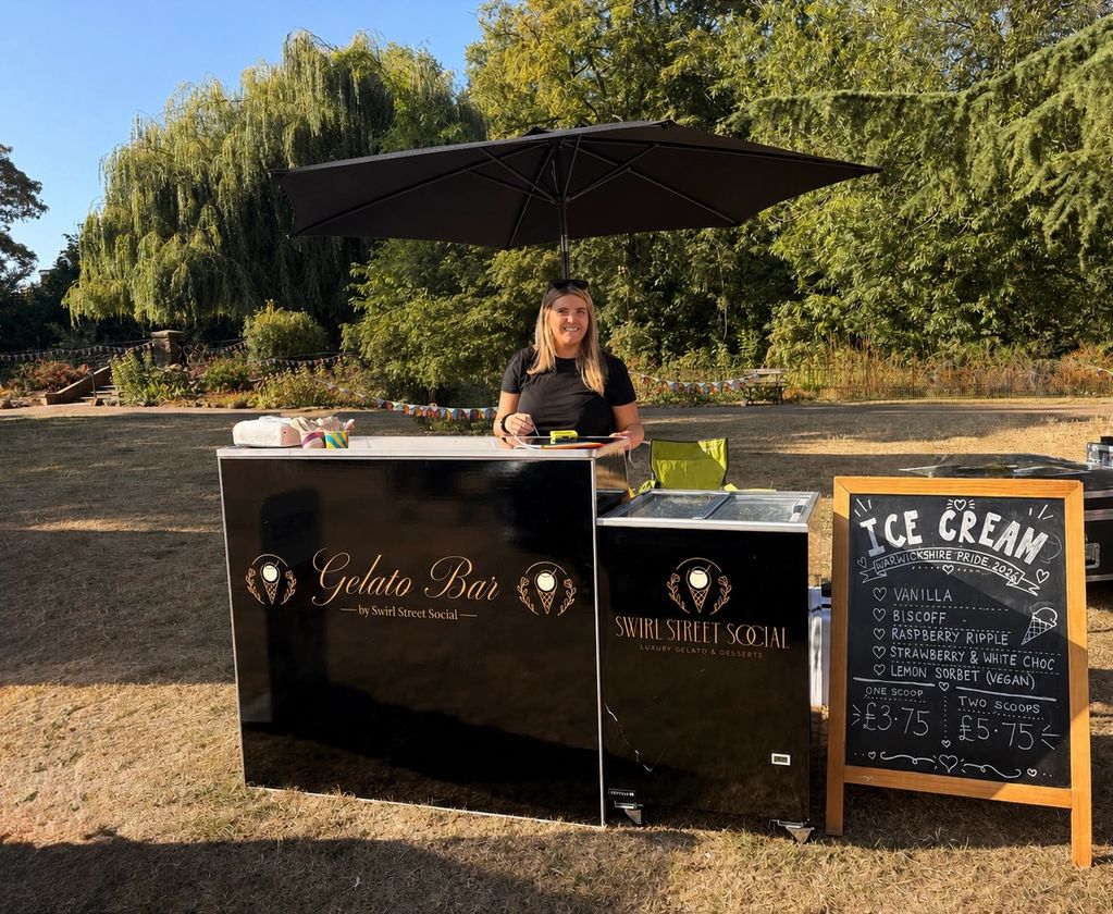 Woman at a gelato bar with an ice cream menu board outdoors.