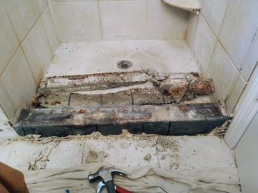 Severely damaged shower curb, showing significant structural failure and water damage along the curb