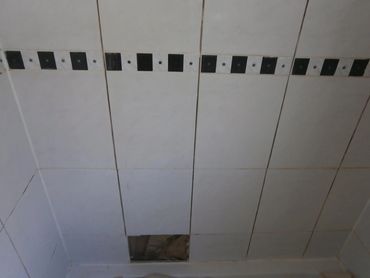 Exposed water damage behind shower tile during grout raking and structural wall repair in Grosse Ile