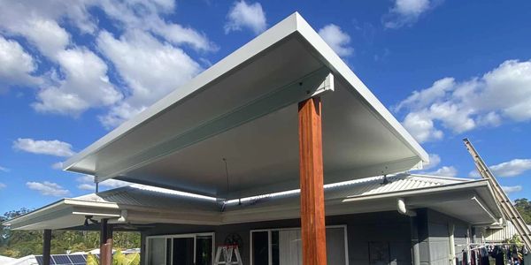 New patio roof installation over wooden deck with blue sky and clouds.