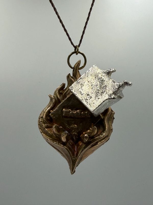 Metal pendant with flame design and silver cube.