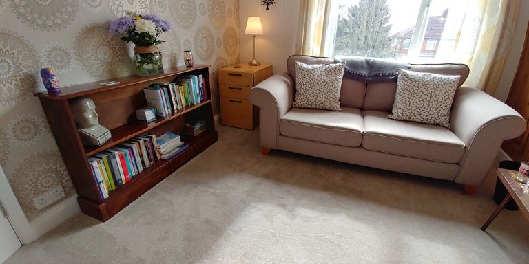 A bright airy therapy room with a light coloured sofa on the right, and a bookcase on the left.