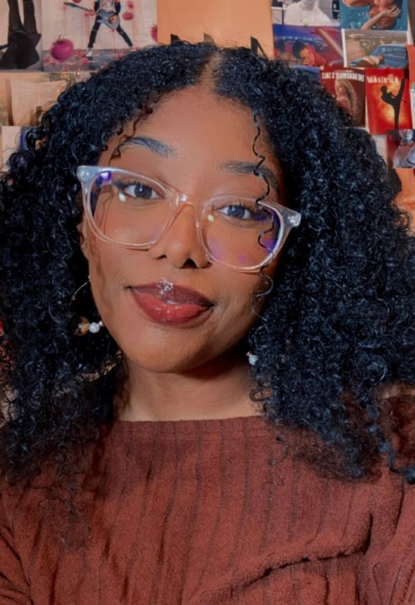 Young woman with curly hair and clear glasses smiling warmly.