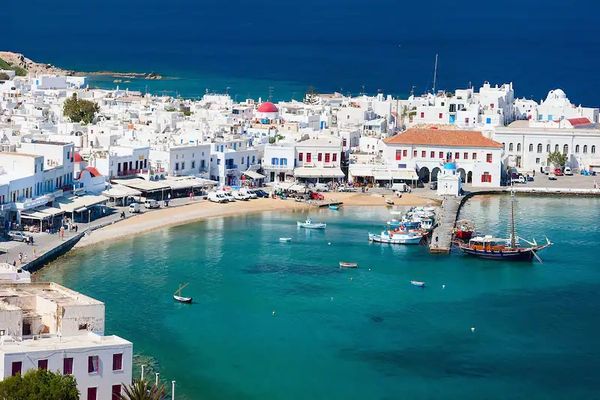Vue d'un port grec avec maisons blanches et mer turquoise.