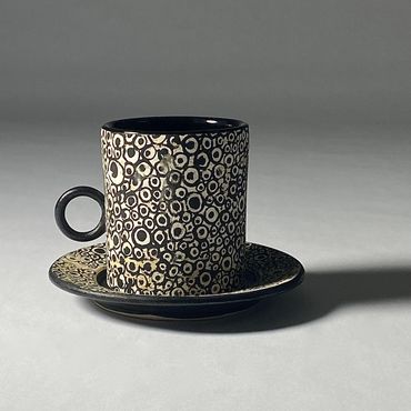 White ceramic espresso cup and saucer with circle and dot design in black. Black handle, interior.