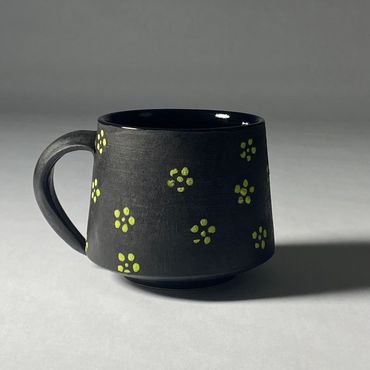 Black ceramic mug with small green flower design. Gloss black interior.