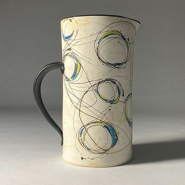 White ceramic pitcher with fluid circular design. Cool color accents. Black handle and interior.