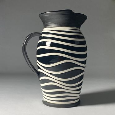 Black and white ceramic pitcher with wavy line design. Black neck, handle, base.
