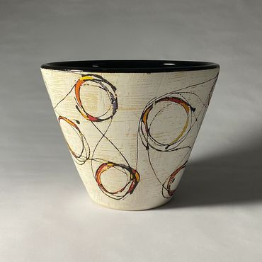 White ceramic serving bowl with fluid circular design. Warm color accents. Black interior.