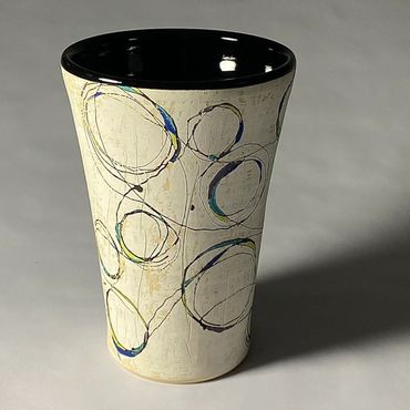 White ceramic vase with fluid circular design. Cool color accents. Black interior.