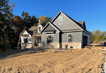 House under construction with workers installing siding and ladders around.