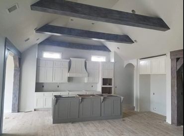 Modern kitchen with white cabinets and gray island under vaulted ceiling with dark beams.