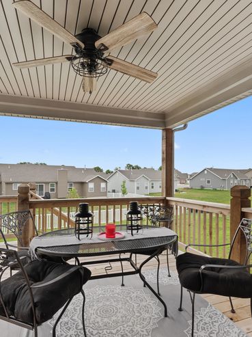 Covered wooden deck with metal furniture and ceiling fan overlooking neighborhood.