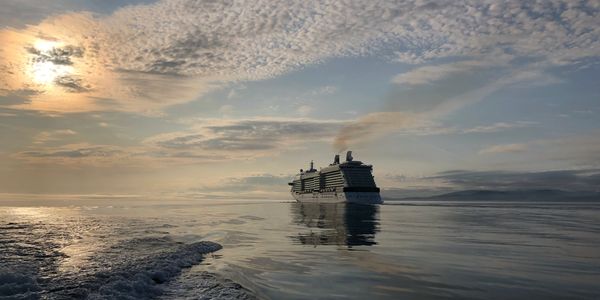 A cruise ship sails on calm waters under a partly cloudy sky at sunset.