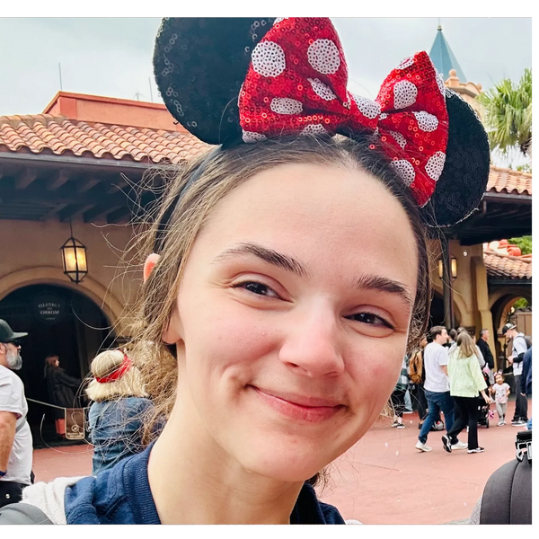 Smiling woman wearing Minnie Mouse ears at a theme park.