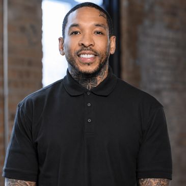 Smiling man in black polo shirt with tattoos.
