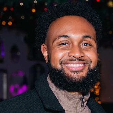 Smiling man with a beard in a dimly lit background.