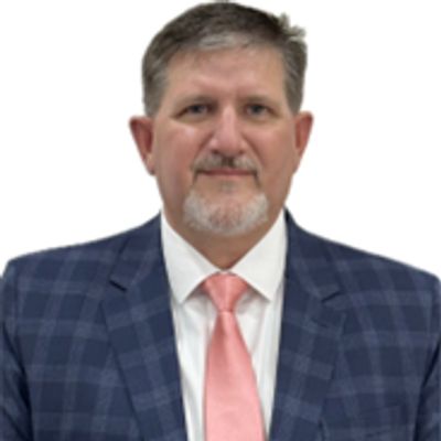 Man in checkered suit and pink tie with light beard.
