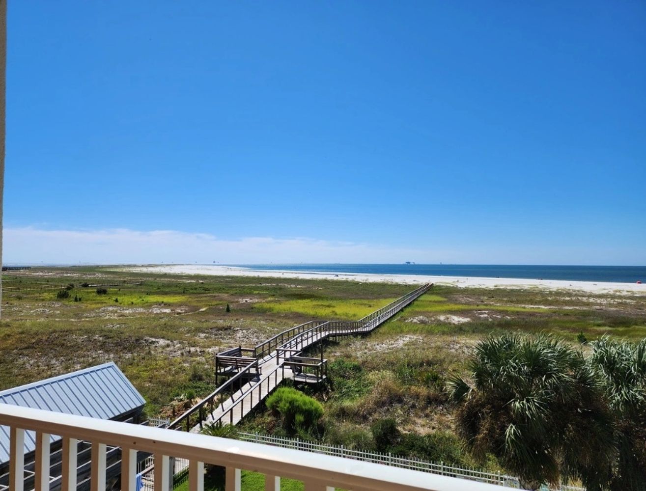 A wooden boardwalk leads to a sandy beach under a clear blue sky.