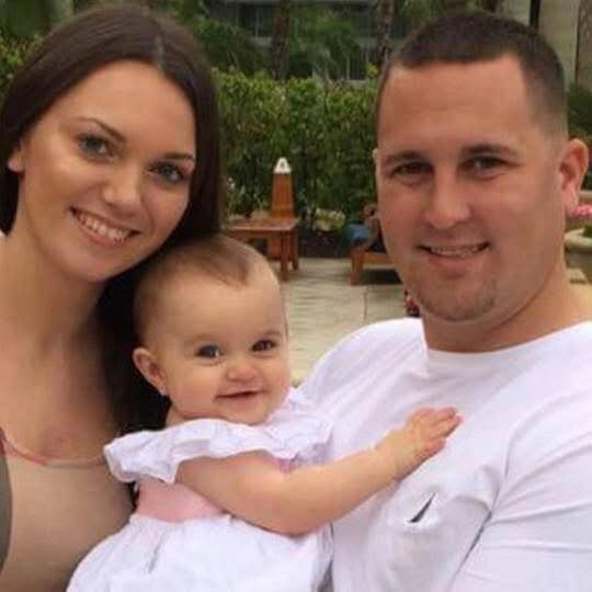 A happy family portrait with a mother, father, and baby smiling outdoors.