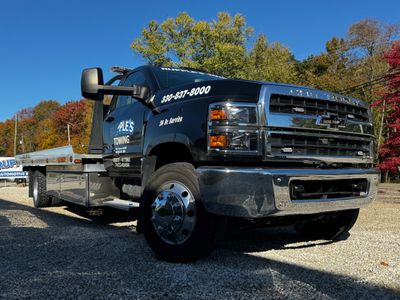 Black Chevrolet flatbed tow truck with company branding and phone number.