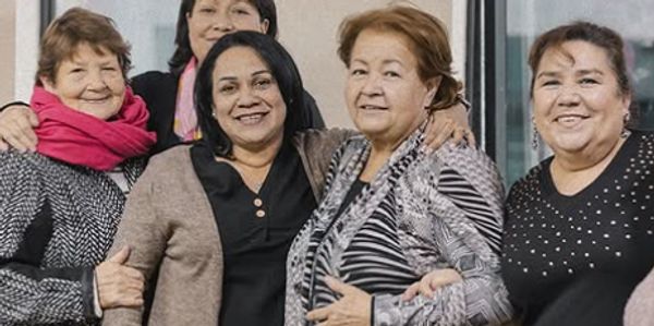 Group of five smiling women posing together indoors.
