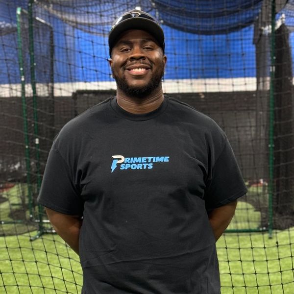Smiling man in a black Primetime Sports t-shirt at an indoor sports facility.
