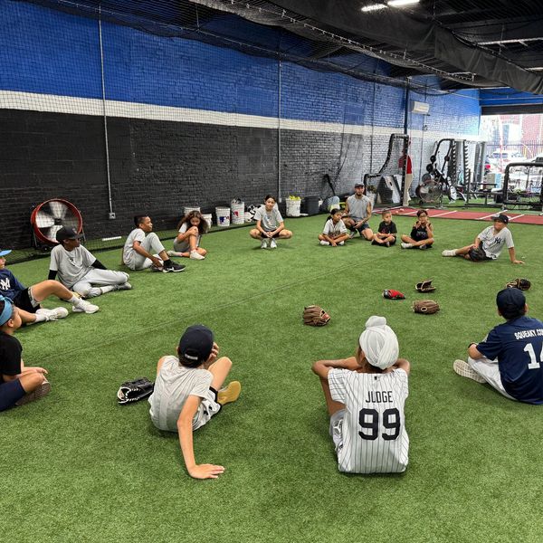 Kids sitting in a circle on turf in an indoor sports facility.