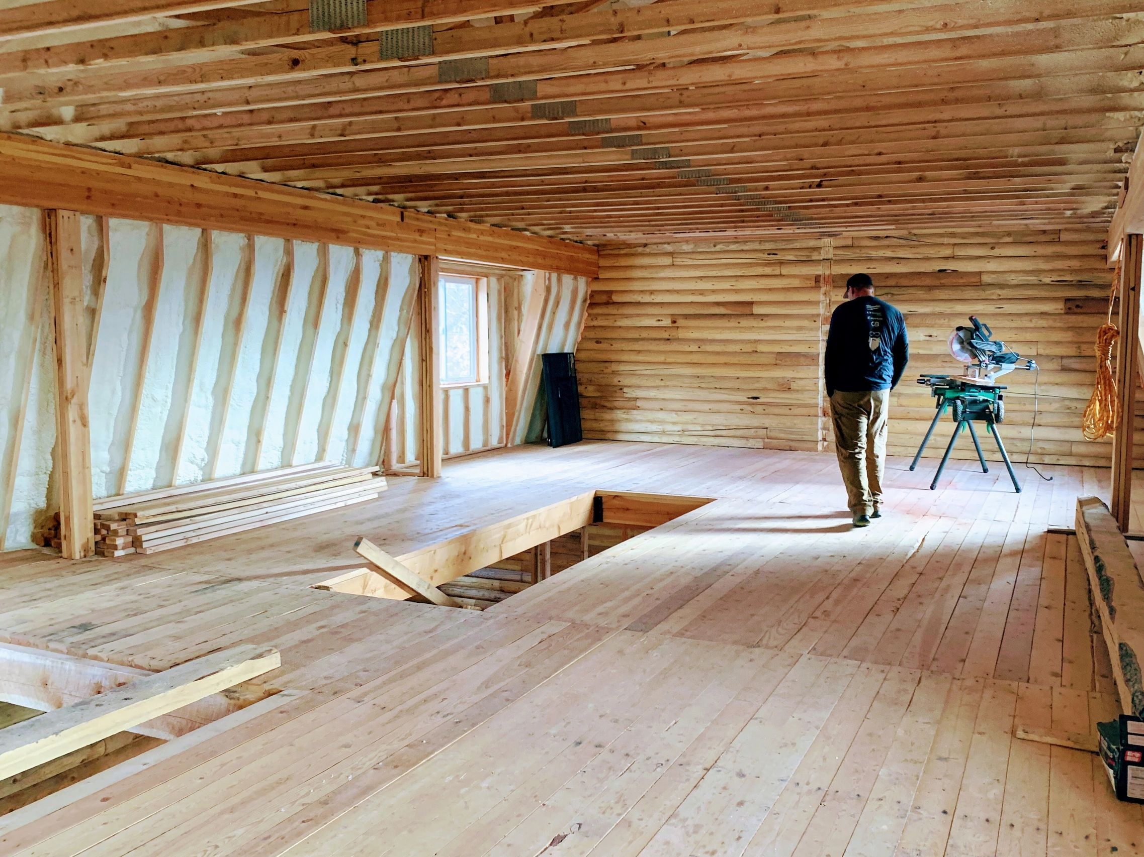 Person walking inside a wooden cabin under construction with tools around.