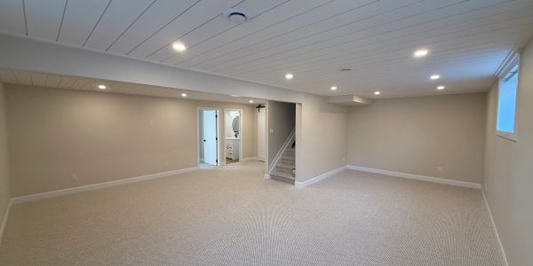 Empty, carpeted basement with recessed lighting and stairs.