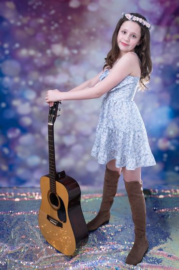 tween girl in blue dress and boots standing with guitar on ground